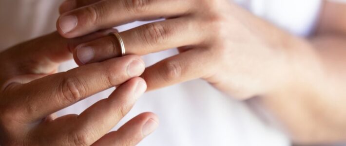 Close-up of hands removing a wedding ring, symbolizing divorce or separation.